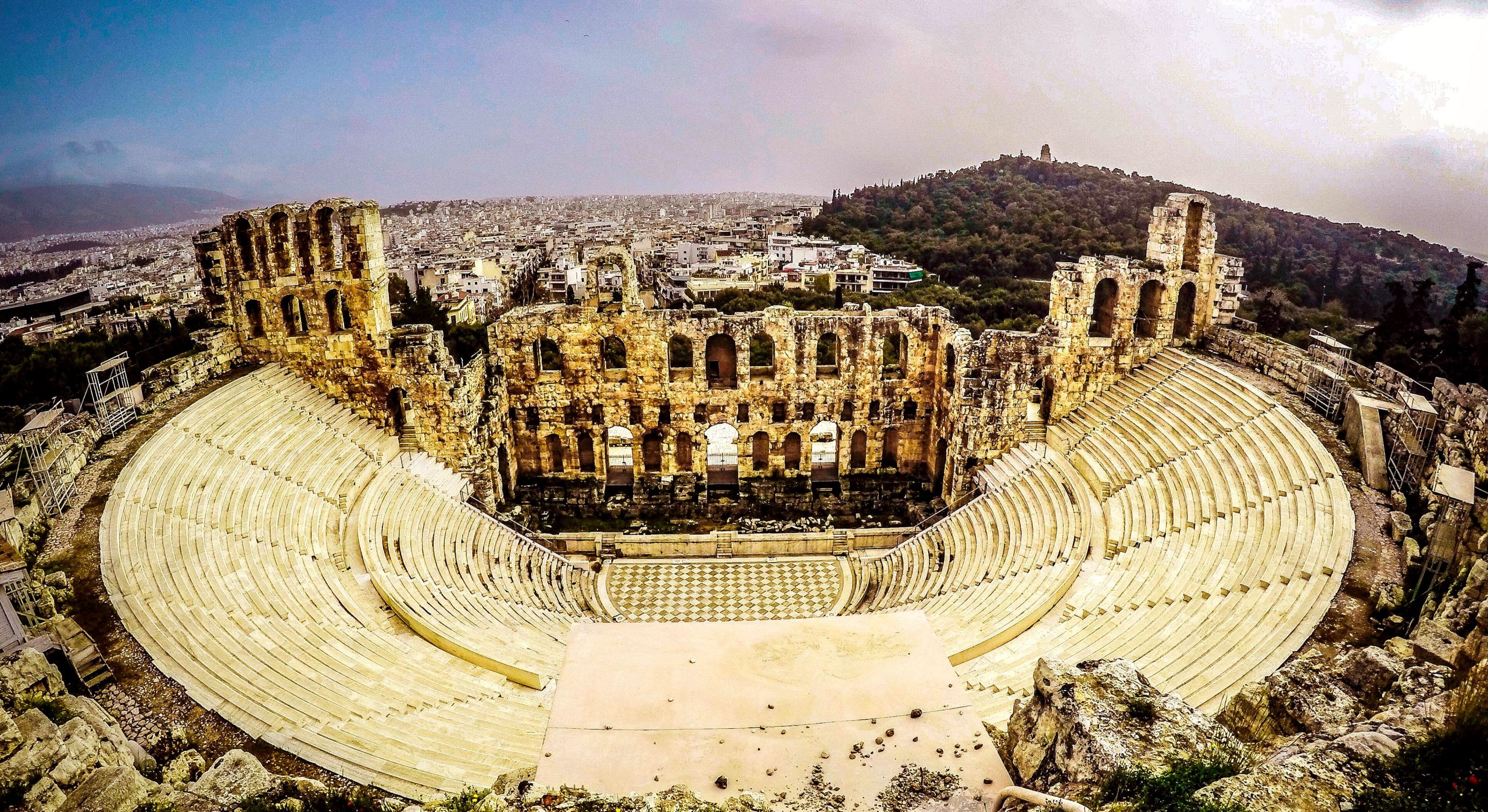 Vista panorámica del teatro romano de Mérida con asientos de piedra y entradas arqueadas, con vistas a una ciudad moderna.