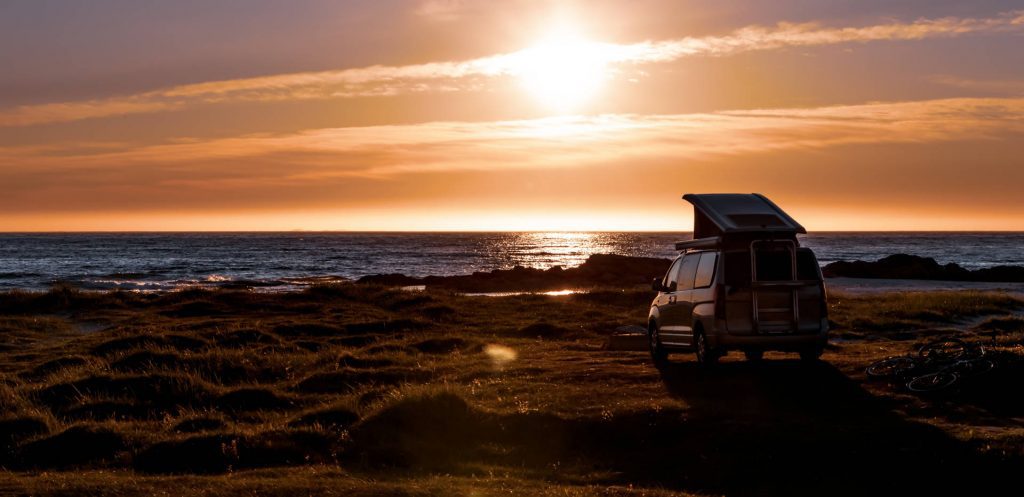 Una autocaravana estacionada en la playa al atardecer durante una pernoctación.
