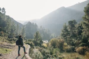 Persona de pie en un sendero, contemplando las pintorescas montañas y árboles bajo un cielo brumoso, con un MAPA turístico de Cataluña en la mano para guiar su viaje.